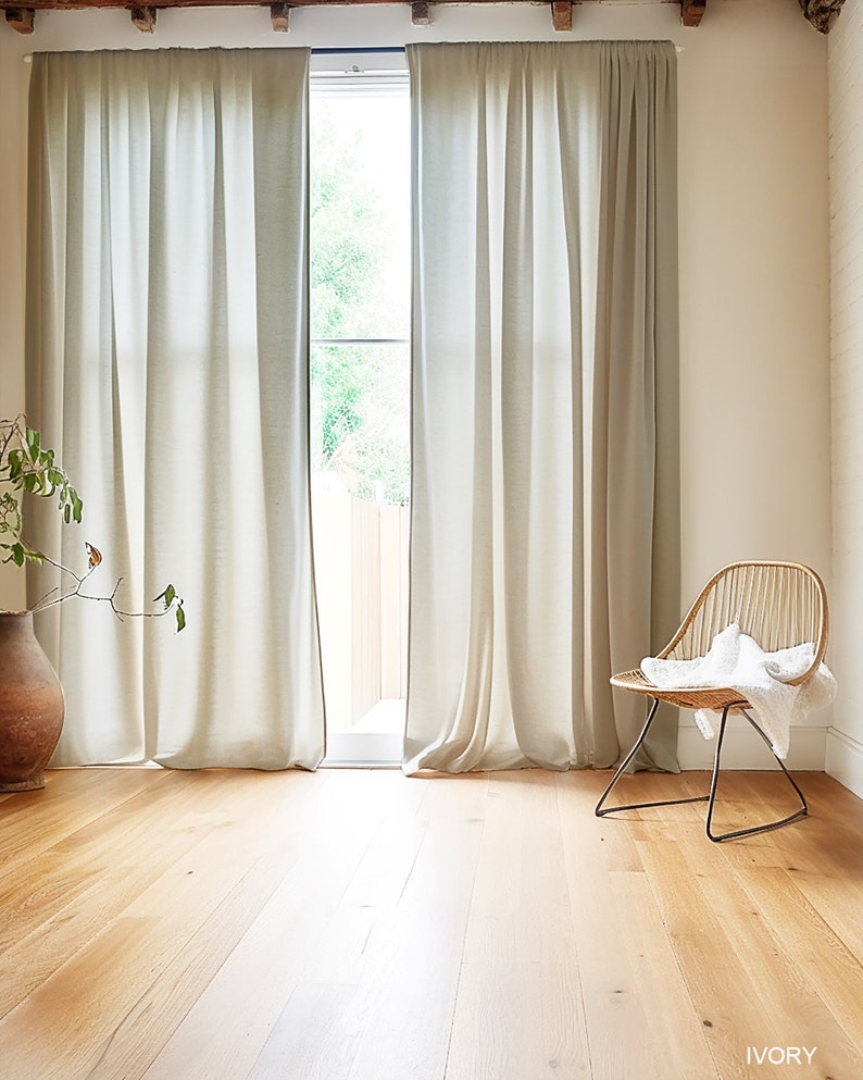 K&ouml;nnte beinhalten: Ein hellbeiger Raum mit einem gro&szlig;en Fenster und wei&szlig;en Vorh&auml;ngen. Der Boden ist aus hellem Holz und in der Ecke des Raumes steht ein Korbstuhl mit einer wei&szlig;en Wolldecke. Der Text "IVORY" ist in der unteren rechten Ecke des Bildes gedruckt.