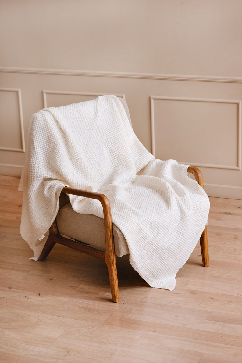 May include: A white waffle weave throw blanket draped over a wooden armchair with a beige fabric seat.