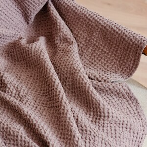 May include: A soft, mauve waffle weave throw blanket draped over a chair.