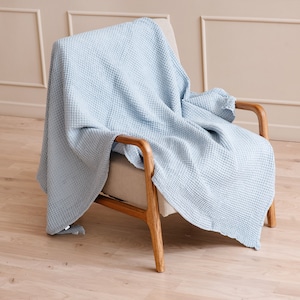 Peut inclure: Une couverture en tissu gaufré bleu clair posée sur un fauteuil en bois avec un coussin beige clair.