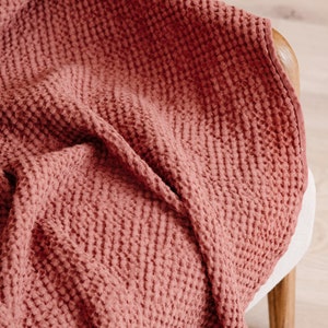 May include: A soft, red waffle weave throw blanket draped over a wooden chair.