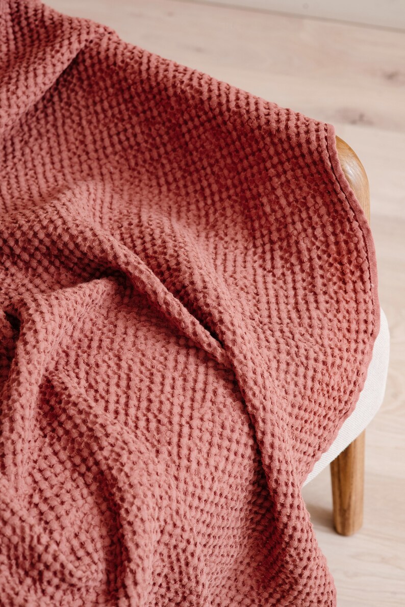 May include: A soft, red waffle weave throw blanket draped over a wooden chair.