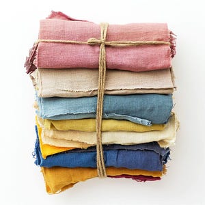 May include: A stack of fabric scraps in various colors, including pink, beige, blue, yellow, and red, tied together with twine.