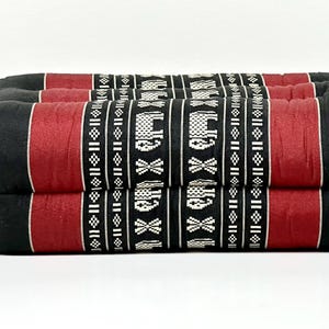 May include: A black and red rectangular floor cushion. The cushion has a central red stripe with a repeating pattern of white elephants and geometric shapes. The sides are black.