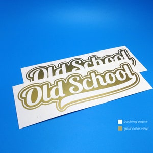 Puede incluir: Dos pegatinas blancas con texto dorado que dice "Old School" en una fuente estilizada. Las pegatinas están sobre un fondo azul. El papel de respaldo es blanco y el vinilo es dorado.