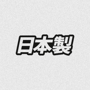 Op de afbeelding: Een zwart-witte sticker met de Japanse kanji-tekens 日本製, wat vertaald Made in Japan betekent. Het ontwerp bestaat uit dikke, zwarte letters met een witte omlijning, gepresenteerd tegen een lichtgrijze, getextureerde achtergrond.