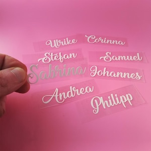 Könnte beinhalten: Ein Satz von acht weißen Vinyl-Namensschildern mit kursiv geschriebener Schrift. Die Namen sind: Ulrike, Corinna, Stefan, Samuel, Sabrina, Johannes, Andrea und Philipp.