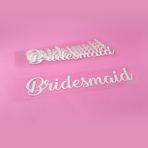 May include: A sheet of white vinyl with the word "bridesmaid" printed on it multiple times. The sheet is on a pink background.