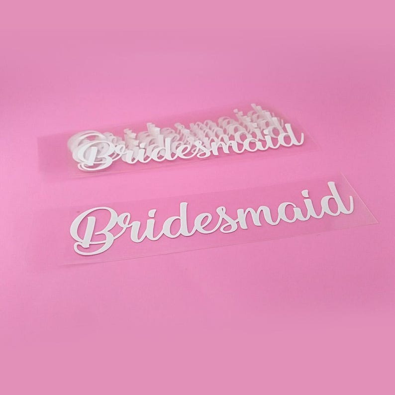 May include: A sheet of white vinyl with the word "bridesmaid" printed on it multiple times. The sheet is on a pink background.