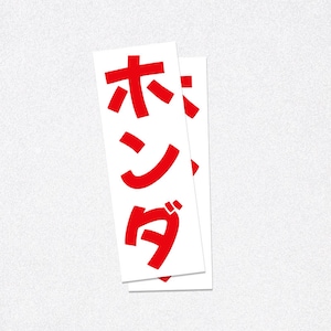 Op de afbeelding: Twee witte rechthoekige stickers met de Japanse karakters voor "Honda" in het rood gedrukt. De stickers overlappen elkaar lichtjes, met de tekst verticaal gericht.