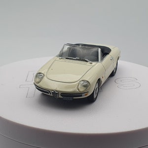 May include: A white toy car model of an Alfa Romeo convertible. The car has a black interior and black wheels.
