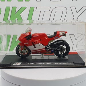 May include: A red and white Ducati Desmosedici motorcycle model, presented in a clear display case. The model features the number 65 on the tail and the text "Ducati Desmosedici Loris Capirossi 2004" on the base. A collectible motorcycle.
