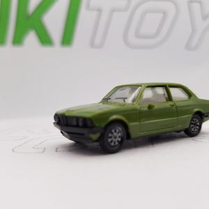 Könnte beinhalten: Ein grünes Spielzeugautomodell eines klassischen Sedans. Das Auto hat eine schwarze Frontstoßstange und schwarze Räder.