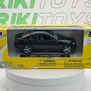 May include: A black BMW 3 Series Coupe die-cast model car in a yellow and white box. The packaging features the text City Cruiser, BMW 3 Series Coupe, 1:43 scale, and warning labels. The car has silver wheels and a detailed exterior design.