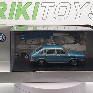 May include: A diecast model of a blue 1968 Volkswagen 411 sedan. The model is displayed in a clear plastic case within a silver box. The box has the Volkswagen logo and the text "RIKI TOYS".