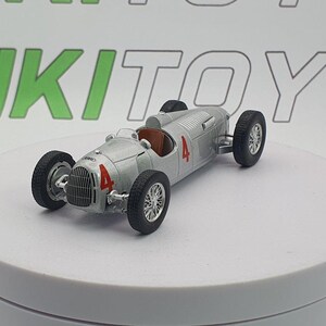 Può includere: Modello di auto da corsa vintage argentata con il numero 4 in rosso sul lato e sulla parte anteriore. L'auto ha pneumatici neri e interni marroni. Il modello è su una superficie bianca con la scritta RIKITOYS in verde sullo sfondo.