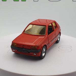 May include: A red toy car model of a Peugeot 205, a popular hatchback car from the 1980s and 1990s.