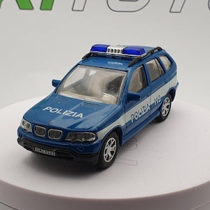 May include: A blue and white die-cast model of an Italian police car. The model features the word "POLIZIA" on the hood and sides, along with a blue light bar on the roof. The car is a BMW X5 model.