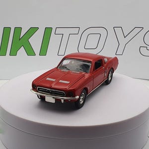 May include: A red 1960s Ford Mustang toy car model. The car is on a white display stand.