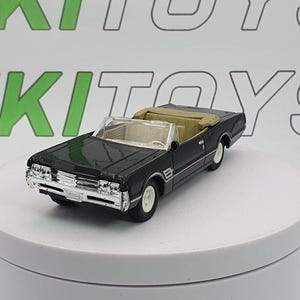 Könnte beinhalten: Ein schwarzes Spielzeug-Cabrio mit beigem Innenraum und Weißwandreifen. Das Auto hat Chromdetails an den vorderen und hinteren Stoßfängern und steht auf einer weißen Oberfläche. Das Auto ist eine Miniatur-Nachbildung eines klassischen Fahrzeugs.