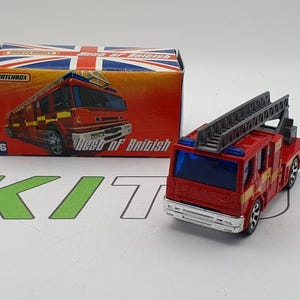 Puede incluir: Un camión de bomberos de juguete rojo y blanco con una escalera y un parabrisas azul. El camión está sobre una superficie blanca. La caja dice "Best of British" y tiene un diseño de bandera de la Union Jack.