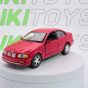 May include: A red die-cast BMW sedan toy car featuring a detailed front grille with the BMW emblem, clear headlights, silver-colored wheels, and black interior details. The vehicle is positioned at an angle, showcasing its side profile and hood.