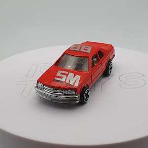 May include: A small, red toy car with silver accents. The car has the number "88" on the roof and the letters "SM" on the hood. The car has black wheels and a silver front bumper. The toy car is a miniature replica of a real car.