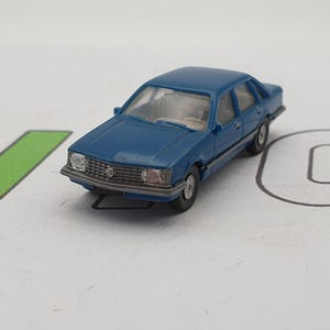 Peut inclure: Une miniature de voiture de tourisme classique bleue. La voiture a une calandre et des phares avant détaillés.