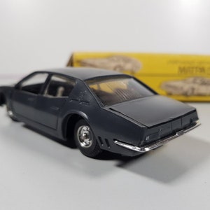 May include: A dark gray toy car model of a vintage sedan. The car has a detailed interior and a chrome bumper. The car is sitting on a white surface.
