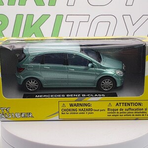 May include: A green die-cast toy car model of a Mercedes Benz B-Class in a yellow and black box. The box has the words "City Cruiser" and "1:43 Scale Die-Cast" printed on it. The box also has a warning label for children under 3 years old.
