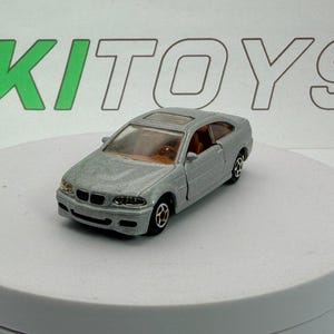 May include: A silver die-cast model car with a sunroof. The toy car has black wheels and a detailed interior. The word "KITOYS" is visible in green and white in the background. The car is on a white surface.