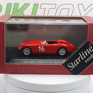 May include: A red 1/18 scale diecast model car of an OSCA MT4 1500 G.P. di Imola 1952 race car. The car has a white number 16 on the side. The car is displayed in a clear plastic case with a red and gold Starline Models box.