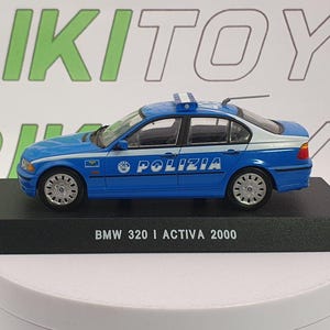 May include: A blue and white diecast model of a BMW 320i police car with the word "POLIZIA" on the side. The model is on a black base and has the text "BMW 320 I ACTIVA 2000".