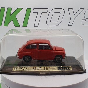 Może przedstawiać: Czerwony model samochodu SEAT 600 w skali 1:18 wykonany z metalu odlewanego ciśnieniowo, umieszczony w przezroczystej plastikowej gablocie. Gablotka ma czarną podstawę z nadrukowanym tekstem "REF 372 SEAT 600 ARTEC".