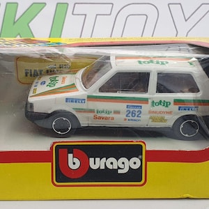 May include: A white Fiat Uno toy car with orange and green stripes and the number 262 on the side. The toy car is in a yellow and red box with the Burago logo.