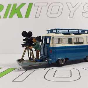May include: A vintage toy van in blue and white with a roof rack, a miniature film camera on a tripod, and a figure of a cameraman. The van has the text "SAMUELSON FILM SERVICE LIMITED" on the side. The word "RIKI TOYS" is in the background.