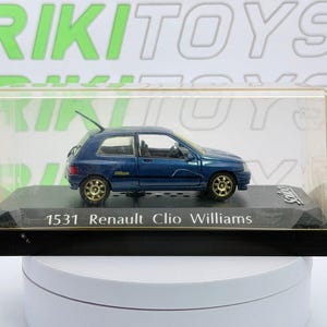 Può includere: Un modellino di auto Renault Clio Williams blu con cerchi dorati, racchiuso in una teca di plastica trasparente su una base nera. La base riporta la scritta 1531 Renault Clio Williams e il marchio Solido stampati in bianco.