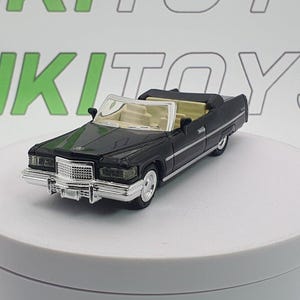 Könnte beinhalten: Ein schwarzes Spielzeug-Cabrio mit silbernem Kühlergrill und Weißwandreifen. Das Auto hat eine beige Innenausstattung und steht vor einem weißen Hintergrund. Das Spielzeugauto ist eine Miniatur-Nachbildung eines klassischen Fahrzeugs.