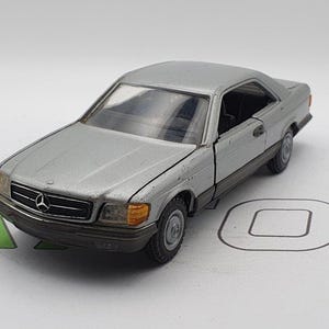 May include: A silver toy car model of a Mercedes-Benz.