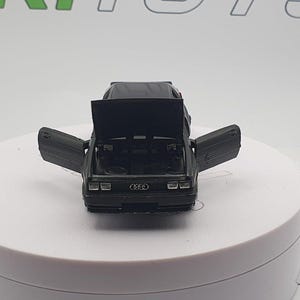 May include: A black toy car model with the doors open, revealing the interior. The car has a black body and a silver grill with the Audi logo.