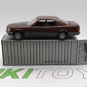 May include: A dark brown toy car model of a Mercedes-Benz on a gray and white cardboard box. The box has the text "Mercedes-Benz" printed on it.