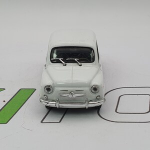 Può includere: Un'auto giocattolo bianca dal design classico, con fari rotondi, un paraurti cromato e tergicristalli. Il veicolo in miniatura è un modello vintage, probabilmente un oggetto da collezione.