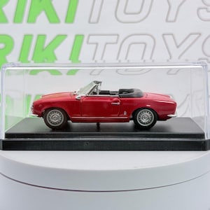 Könnte beinhalten: Ein rotes Cabriolet-Modellauto mit schwarzem Innenraum und silbernen Rädern, präsentiert in einer durchsichtigen Kunststoff-Schutzhülle auf einem schwarzen rechteckigen Sockel. Im Hintergrund ist der grüne Text RIKITOYS zu sehen.