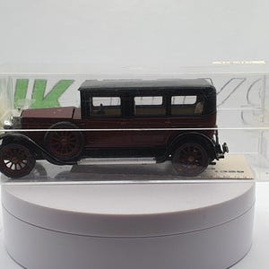 Op de afbeelding: Een donkerrood vintage automodel in een transparante plastic vitrine. De auto heeft een zwart dak en zwarte wielen.