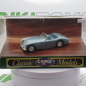 May include: A light blue classic car model in a clear plastic display case with a wooden base. The case has a label that reads "Classic Corgi Models".