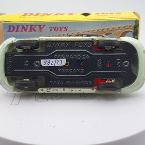 Può includere: Un'auto giocattolo verde con ruote nere e una base rosso e nera. La base ha il testo "Dinky Toys", "Panhard 24", "982/23", "Meccano" e "Made in France".