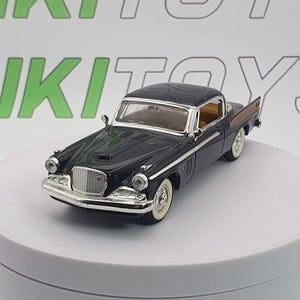 Könnte beinhalten: Ein schwarzes und verchromtes Oldtimer-Modellauto mit Weißwandreifen. Das Auto hat eine beige Innenausstattung und einen detaillierten Frontgrill. Das Modell wird auf einer weißen Drehplattform ausgestellt. Der Text "RIKI TOYS" ist im Hintergrund sichtbar.