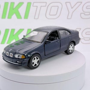 May include: A dark blue BMW sedan die-cast model car featuring silver wheels, clear headlights, and a detailed interior. The vehicle is positioned on a white circular display stand against a white background with the text RIKITOYS visible.