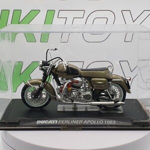 May include: A gold-coloured Ducati Berliner Apollo 1963 motorcycle model in a clear display case. The motorcycle has a black seat and black wheels.