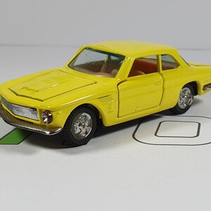 May include: A yellow toy car model with a black grill and black wheels. The car has a detailed interior and a black windshield.